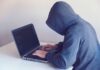 Haker w kapturze pracujący przy netbooku w jasnym pokoju