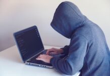Haker w kapturze pracujący przy netbooku w jasnym pokoju