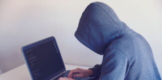 Haker w kapturze pracujący przy netbooku w jasnym pokoju