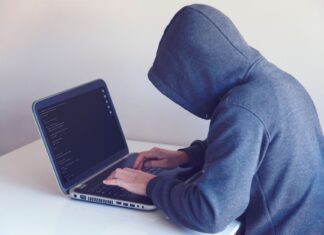 Haker w kapturze pracujący przy netbooku w jasnym pokoju