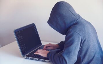 Haker w kapturze pracujący przy netbooku w jasnym pokoju