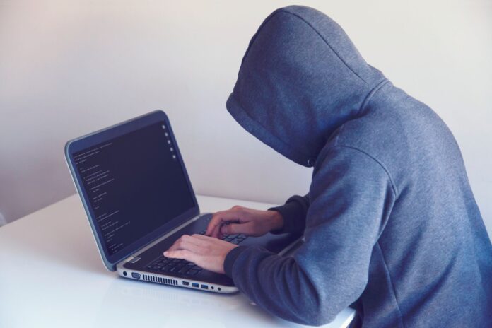 Haker w kapturze pracujący przy netbooku w jasnym pokoju