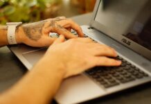 Wytatuowane dłonie piszące na klawiaturze laptopa z Linuxem