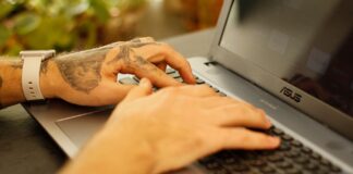 Wytatuowane dłonie piszące na klawiaturze laptopa z Linuxem