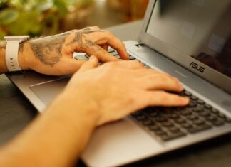 Wytatuowane dłonie piszące na klawiaturze laptopa z Linuxem