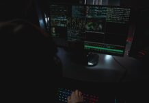 Dlaczego kopie zapasowe nie uratowały tych firm przed ransomware i jak nie powtórzyć ich historii Monitory z kodem w ciemnym pokoju, motyw cyberbezpieczeństwa