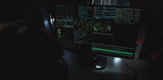 Monitory z kodem w ciemnym pokoju, motyw cyberbezpieczeństwa