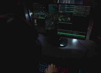 Monitory z kodem w ciemnym pokoju, motyw cyberbezpieczeństwa