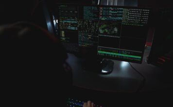 Monitory z kodem w ciemnym pokoju, motyw cyberbezpieczeństwa