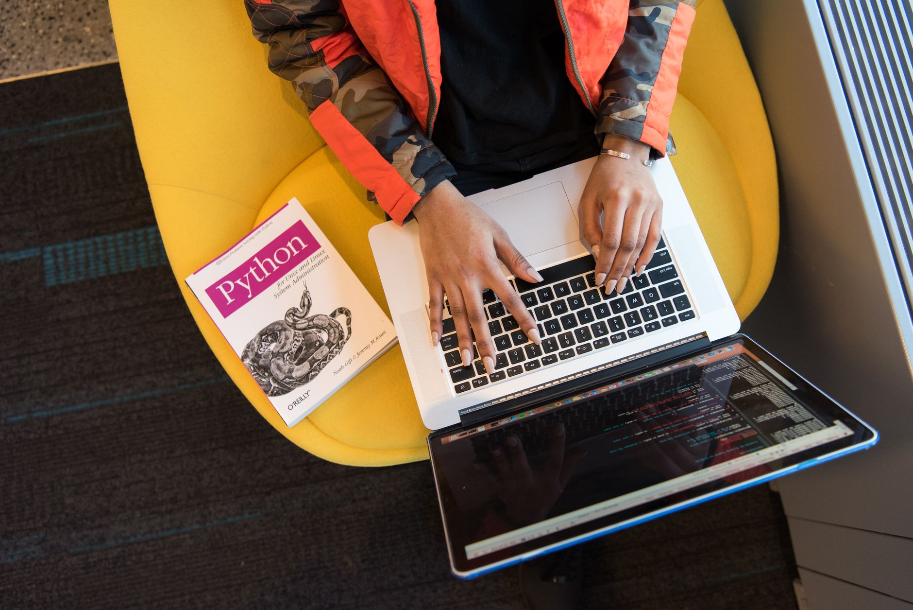 Programista pisze kod na laptopie obok książki o Pythonie